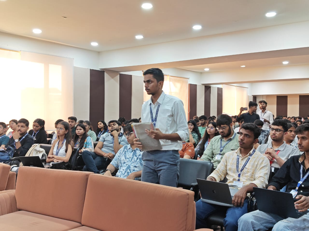 A student standing among a seated audience to ask a question during a Q&A session